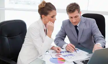 A man and woman professional looking at spreadsheets within an office setting