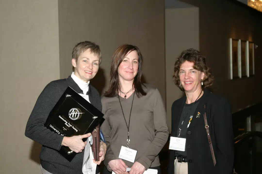 Three women smiling in professional dress. One is holding an American Humanics branded notebook