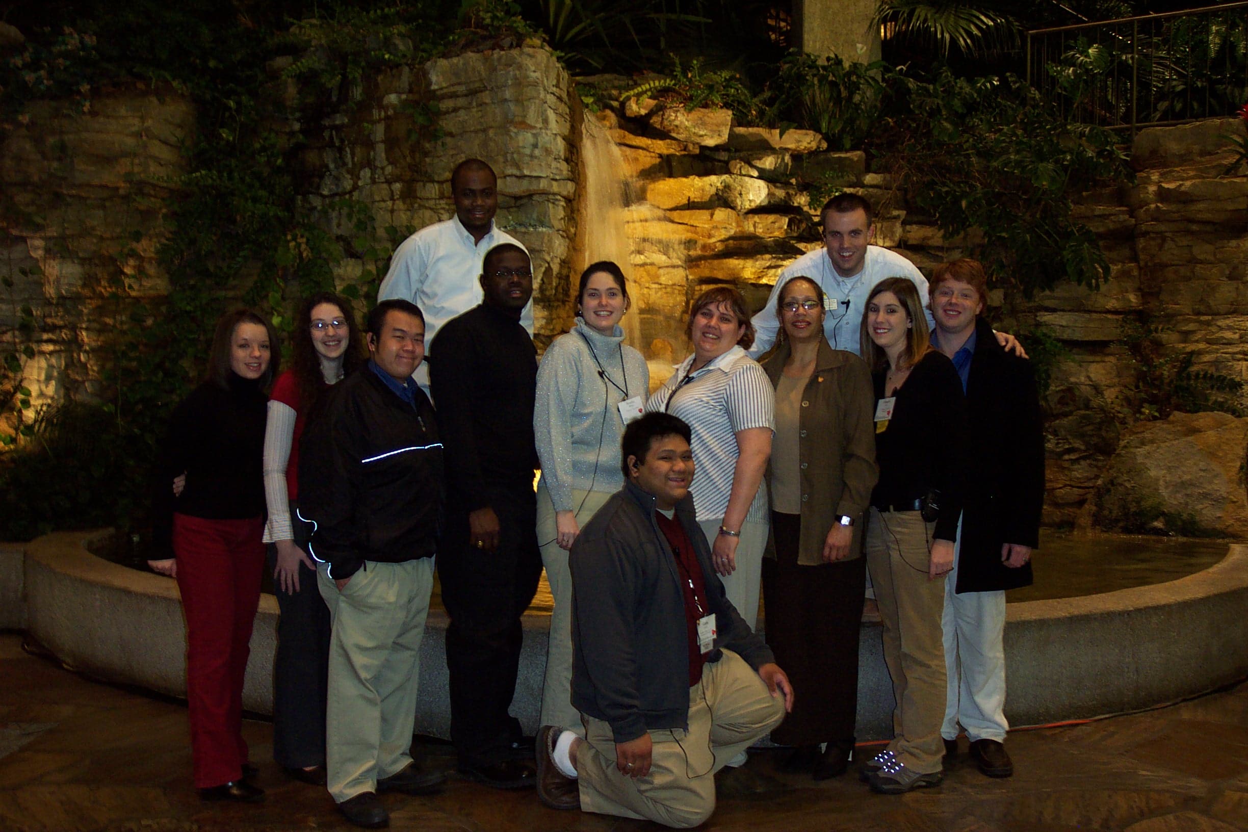 Large group inside smiling in front of a man made water fountain