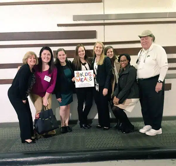 Group of nonprofit professionals holding up a sign that says "Kids Meals"