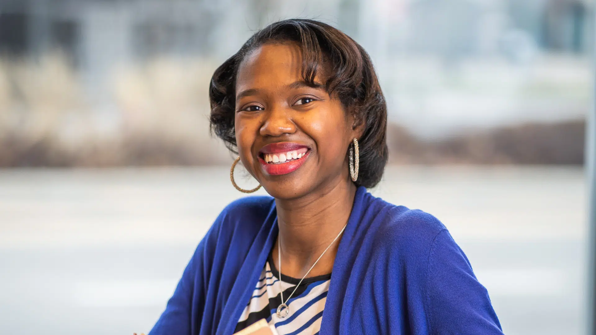 Detriot top nonprofit professional, Charnae Sanders smiling in an office while wearing a black and white blouse and purple cardigan