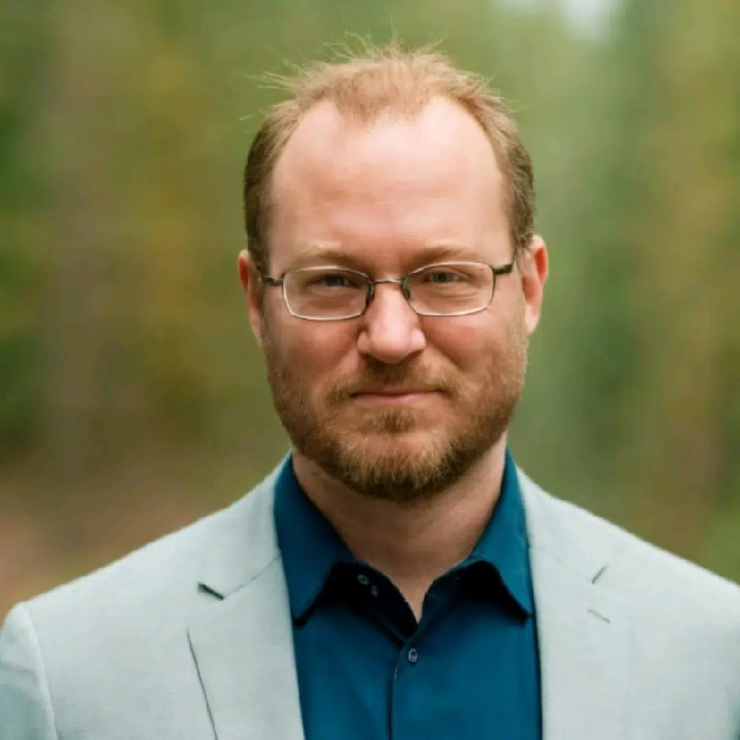 Caucasian Man outside smiling in a grey blazer and blue button down