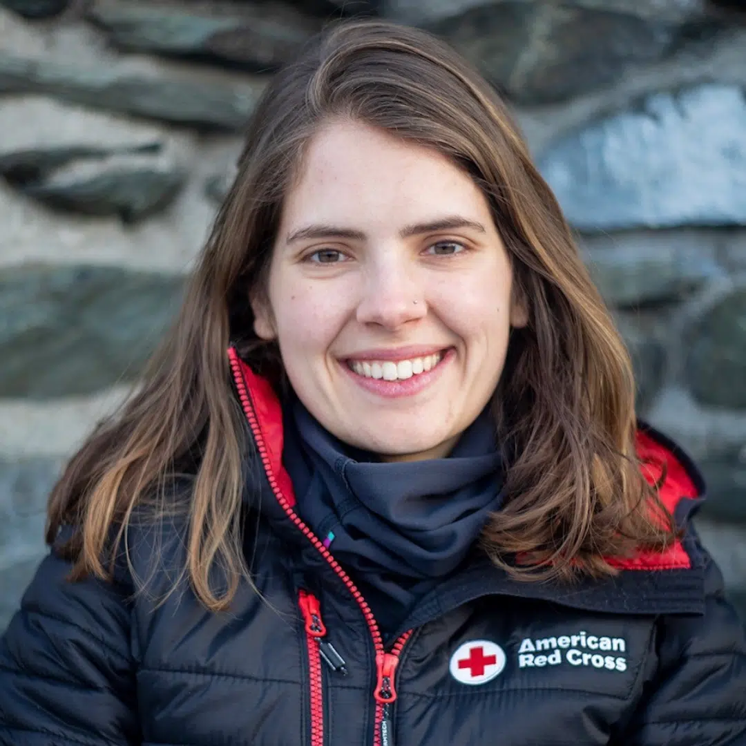 Americorps NCCC Service Year Alumni, Erica Fuller, CNP smiling outside with brunette hair and a black and red American Red Cross branded jacket zipped up