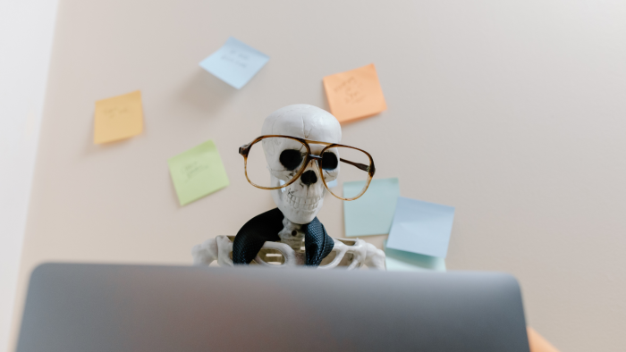 Fake skeleton sitting at a workplace desk with glasses on. The skeleton got burnt out at their job instead of creating a sustainable organizational culture