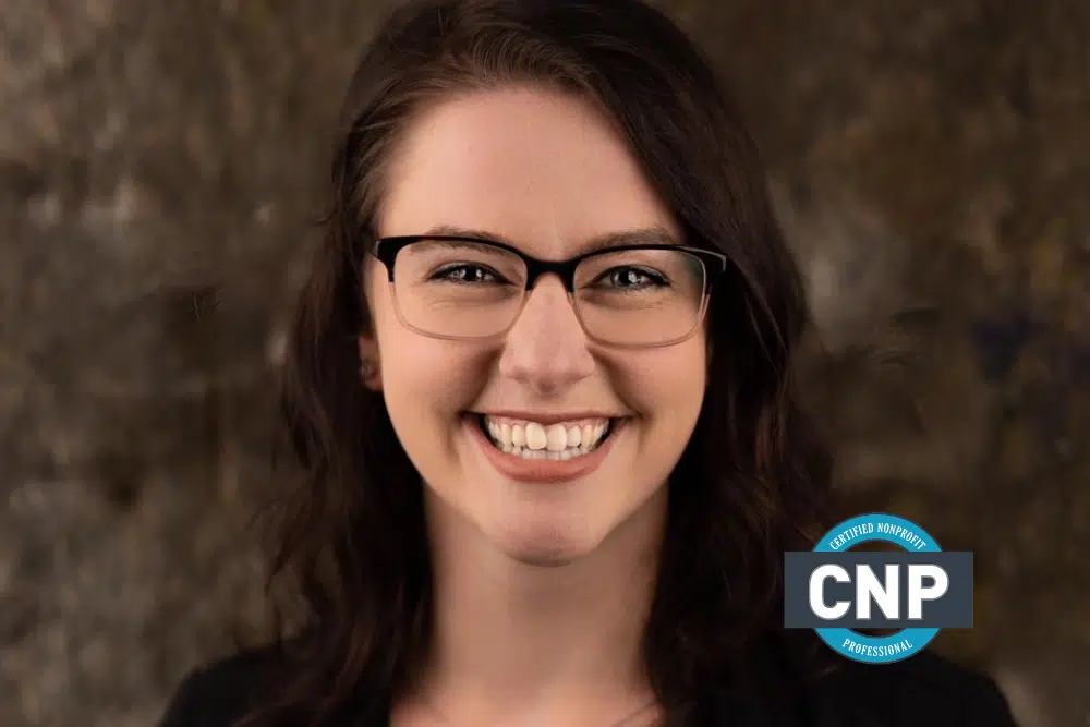 Tracy Kamen, Caucasian woman with dark brown hair smiling brightly with a brown background