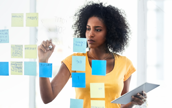 African American woman writing on an office wall covered in sticky notes creating a marketing plan for membership renewal