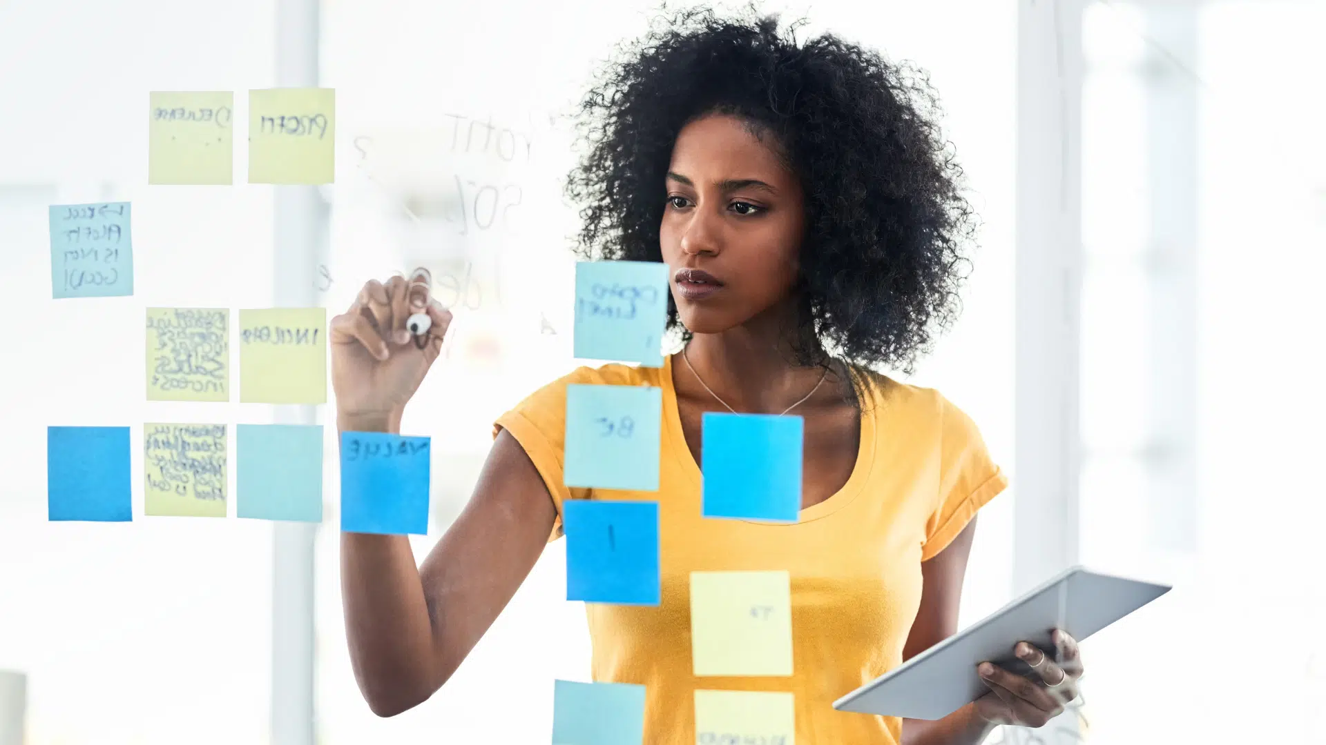 African American woman writing on an office wall covered in sticky notes creating a marketing plan for membership renewal