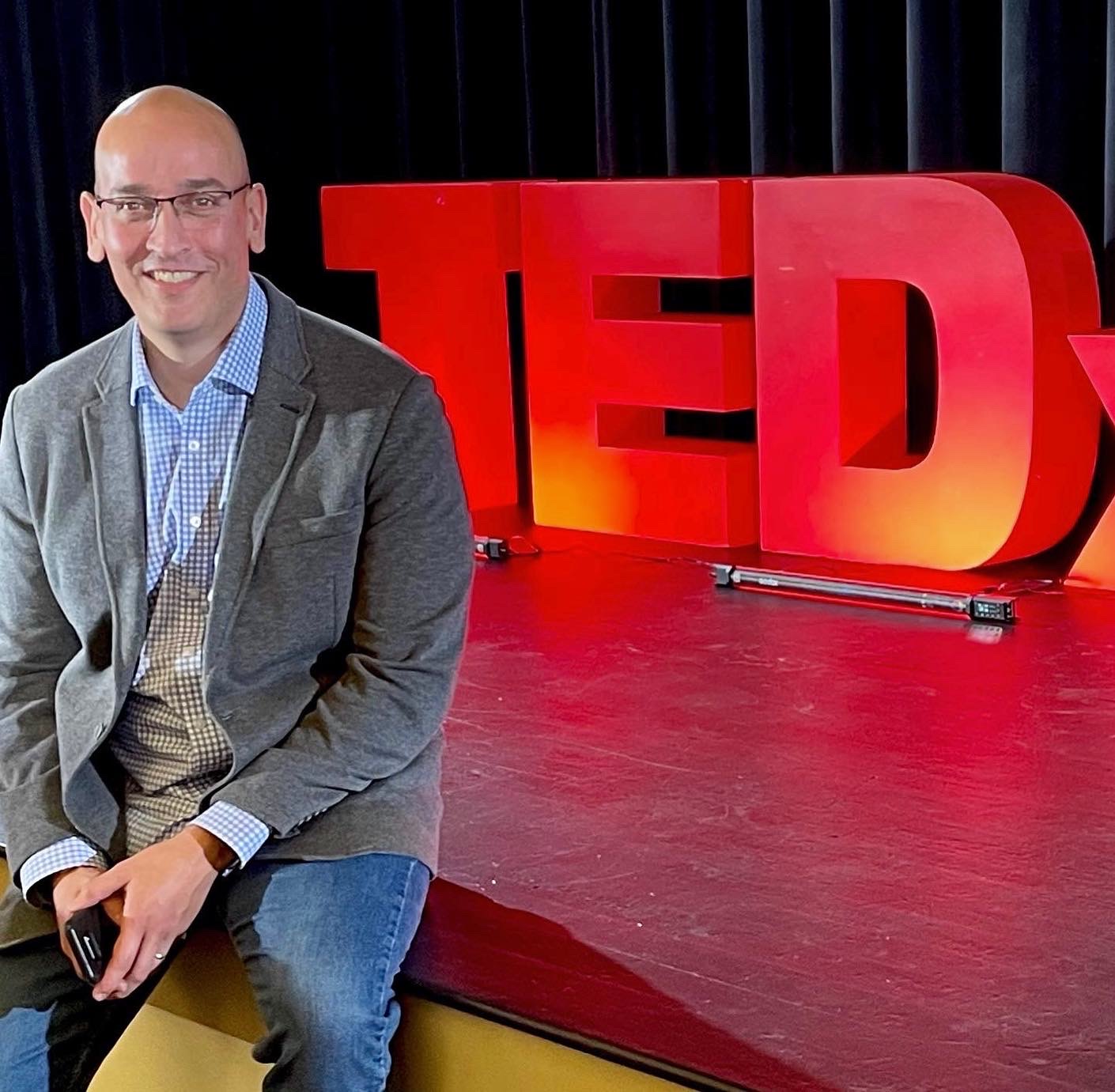 Ian Adair, ACNP, posing in front of a TEDX Stage